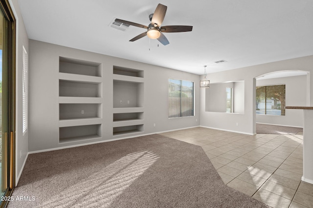 unfurnished living room with built in shelves, ceiling fan, and light carpet