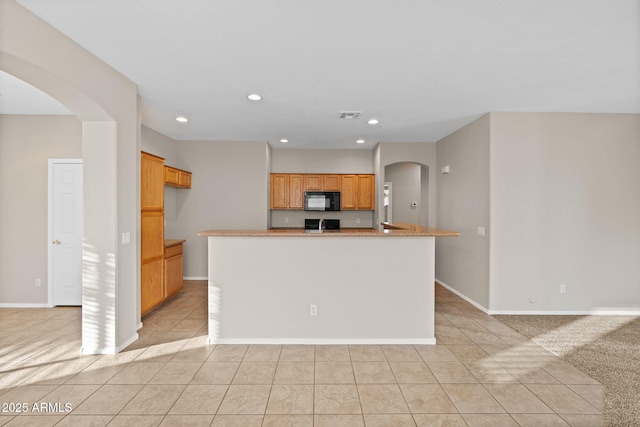 kitchen with a kitchen island with sink, light tile patterned floors, and light stone counters