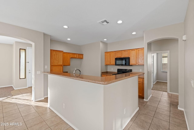 kitchen with stove, a center island with sink, and light tile patterned floors