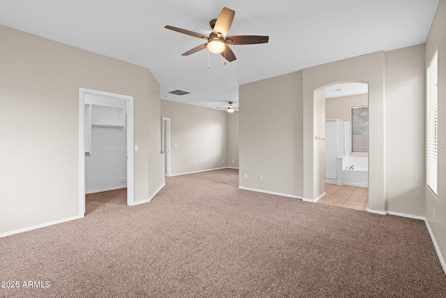 unfurnished bedroom featuring ceiling fan, light colored carpet, a walk in closet, connected bathroom, and a closet