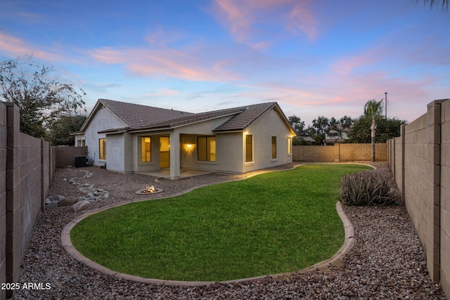 back house at dusk featuring a yard, cooling unit, and a patio