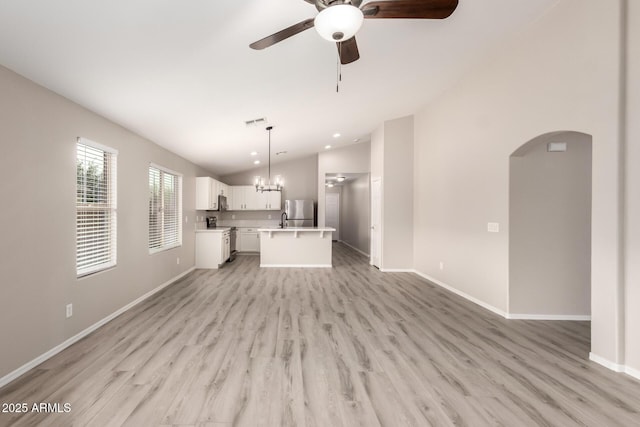 unfurnished living room featuring vaulted ceiling, ceiling fan with notable chandelier, and light hardwood / wood-style flooring