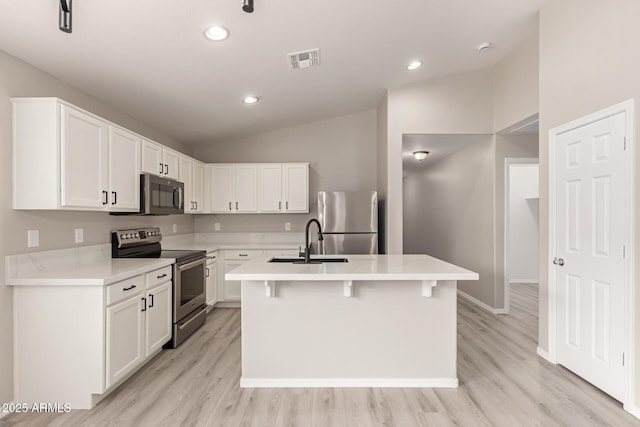 kitchen featuring white cabinets, lofted ceiling, stainless steel appliances, sink, and a center island with sink