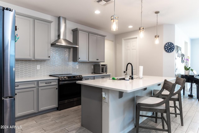 kitchen with electric stove, a center island with sink, stainless steel refrigerator, and wall chimney exhaust hood