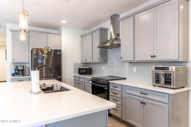 kitchen featuring gray cabinetry, hanging light fixtures, stainless steel refrigerator, electric stove, and wall chimney range hood