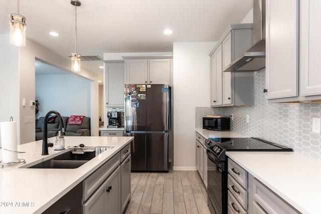 kitchen with sink, tasteful backsplash, black appliances, decorative light fixtures, and wall chimney exhaust hood