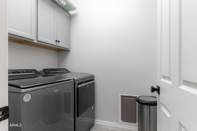 clothes washing area with separate washer and dryer and cabinets