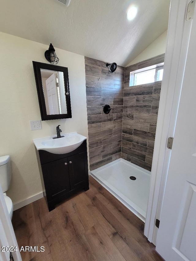 bathroom with tiled shower, toilet, vaulted ceiling, vanity, and hardwood / wood-style flooring