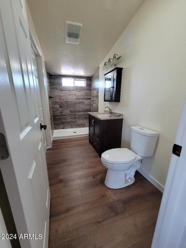 bathroom with toilet, a textured ceiling, a tile shower, vanity, and hardwood / wood-style flooring