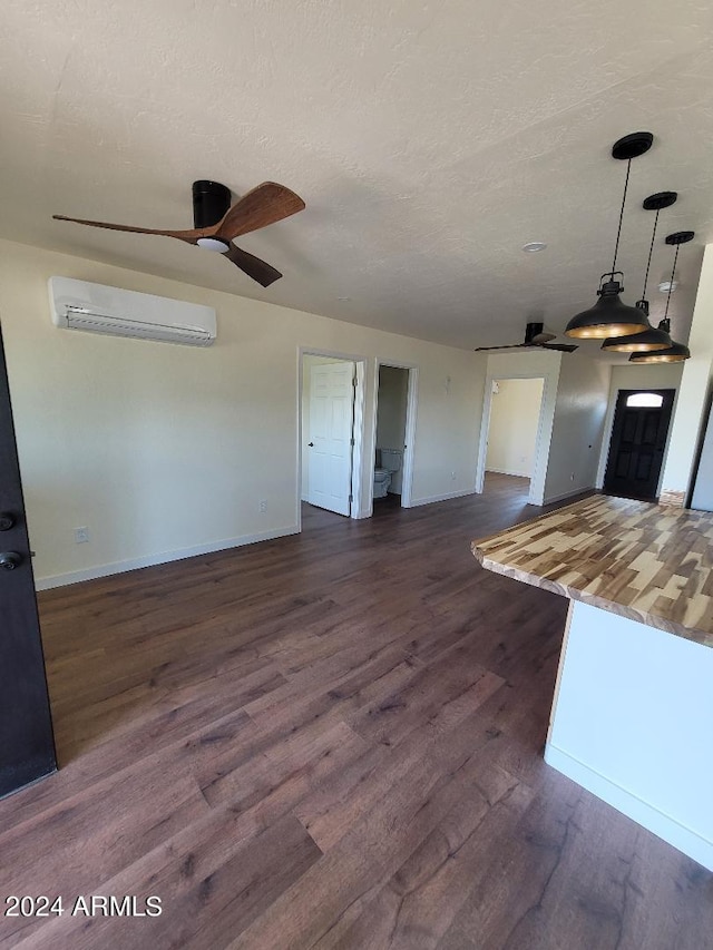 unfurnished living room with dark hardwood / wood-style flooring, ceiling fan, a wall unit AC, and a textured ceiling