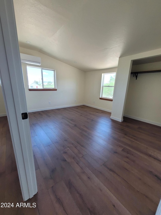 unfurnished bedroom featuring vaulted ceiling, a wall mounted AC, and dark hardwood / wood-style flooring