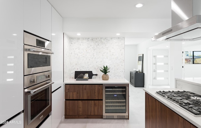 kitchen featuring appliances with stainless steel finishes, dark brown cabinets, exhaust hood, white cabinets, and beverage cooler