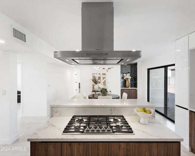 kitchen with island range hood, light stone countertops, dark brown cabinets, and stainless steel gas stovetop