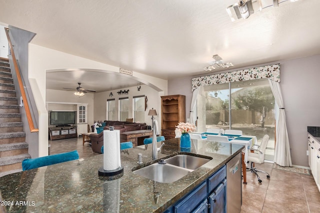 kitchen featuring light tile patterned floors, ceiling fan, blue cabinetry, dark stone counters, and sink