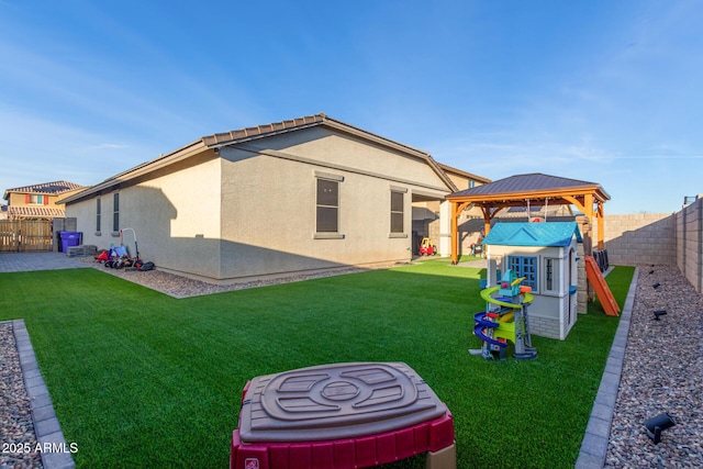 rear view of property featuring a gazebo, a lawn, a fenced backyard, and stucco siding