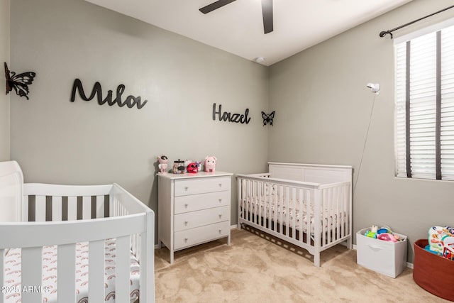 carpeted bedroom featuring ceiling fan and a nursery area