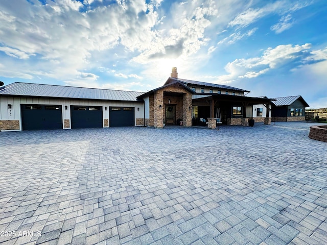 exterior space with stone siding, decorative driveway, a chimney, and an attached garage