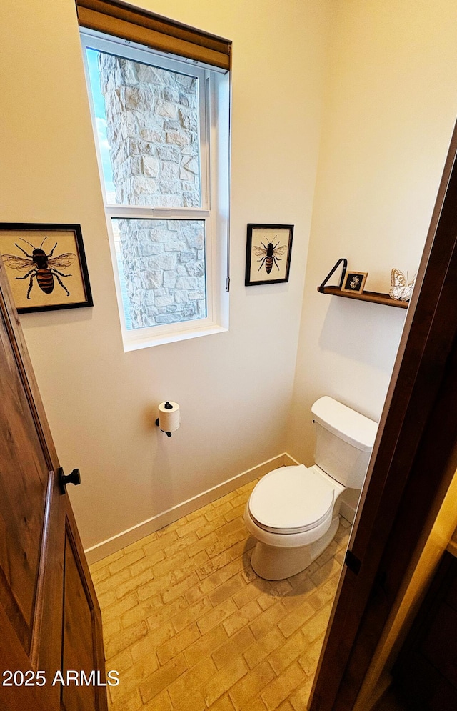bathroom featuring baseboards, toilet, and brick floor