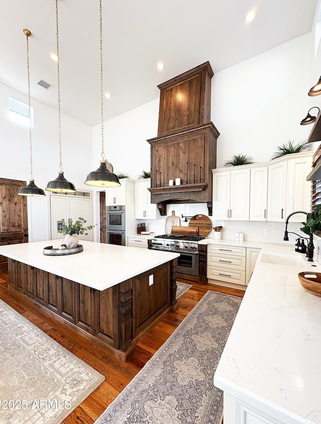 kitchen with a sink, visible vents, dark wood-style flooring, a kitchen island, and appliances with stainless steel finishes