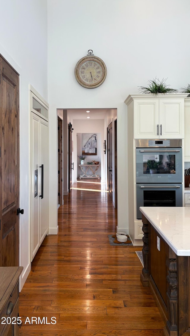 hallway featuring baseboards, dark wood-style flooring, and a towering ceiling