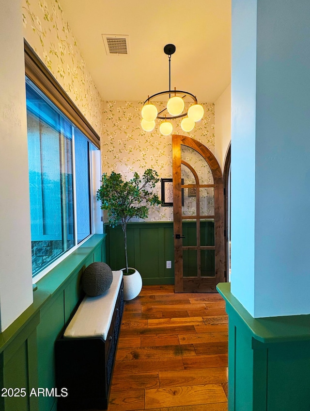 interior space featuring a wainscoted wall, wood finished floors, visible vents, arched walkways, and wallpapered walls