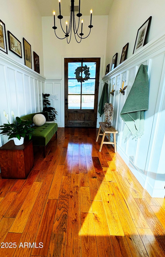 entrance foyer with wainscoting, an inviting chandelier, wood-type flooring, a decorative wall, and a towering ceiling