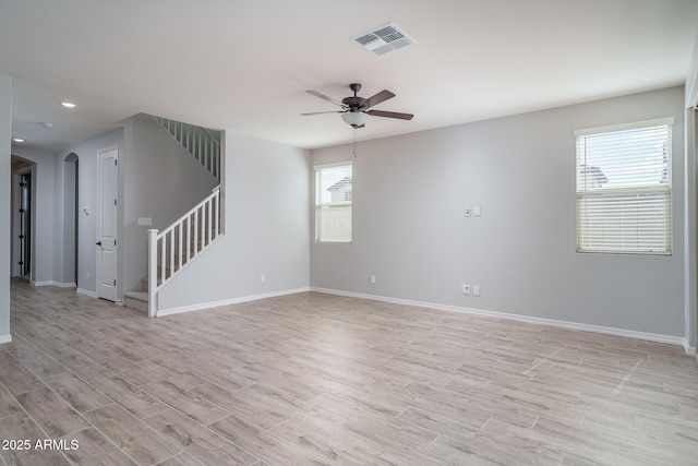 empty room with stairs, light wood finished floors, visible vents, and baseboards