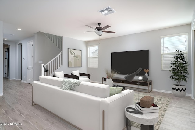 living room featuring arched walkways, visible vents, light wood-type flooring, baseboards, and stairs