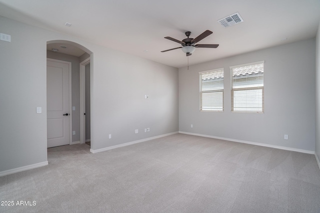 spare room featuring arched walkways, light carpet, visible vents, baseboards, and a ceiling fan