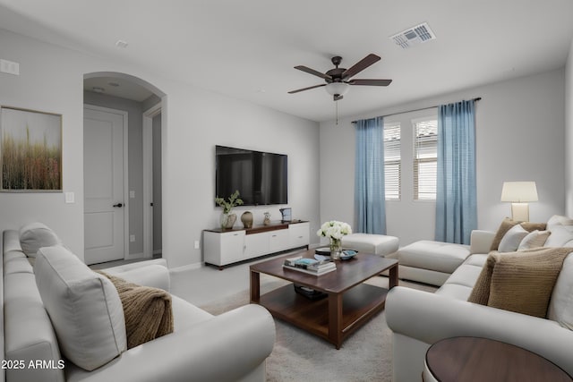 living area featuring visible vents, arched walkways, baseboards, light colored carpet, and ceiling fan