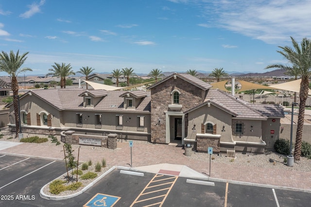 view of front of home with stone siding, a tile roof, uncovered parking, and stucco siding