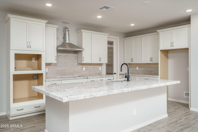 kitchen with an island with sink, a sink, visible vents, and white cabinets