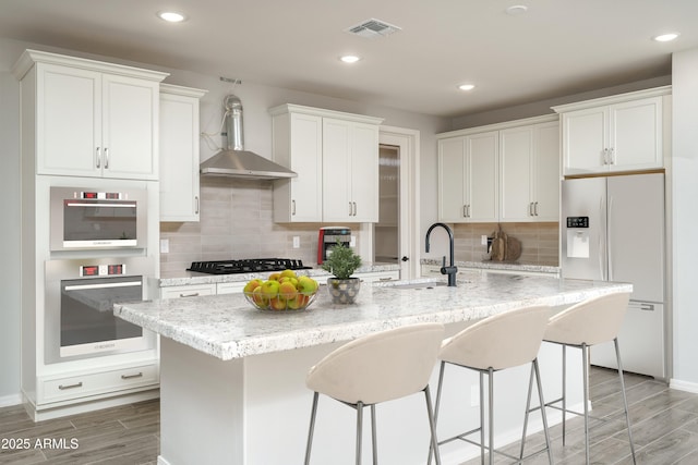 kitchen featuring white fridge with ice dispenser, an island with sink, a sink, and visible vents