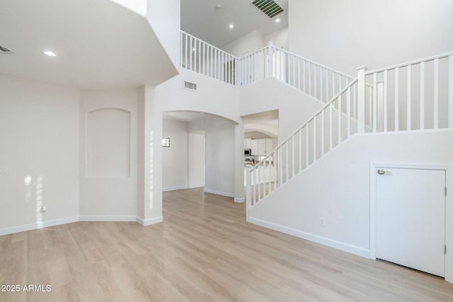 4389 E Muirfield St, Gilbert, AZ 85298 - unfurnished living room with a towering ceiling, stairway, visible vents, arched walkways, and wood finished floors