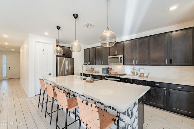 kitchen featuring visible vents, a sink, appliances with stainless steel finishes, a breakfast bar area, and decorative backsplash