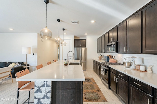 kitchen with a kitchen bar, visible vents, tasteful backsplash, appliances with stainless steel finishes, and dark brown cabinets