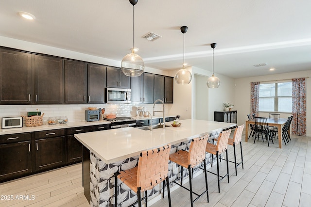 kitchen featuring a breakfast bar area, visible vents, a sink, appliances with stainless steel finishes, and backsplash