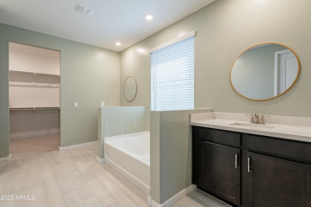 full bathroom with vanity, baseboards, visible vents, a walk in closet, and a garden tub