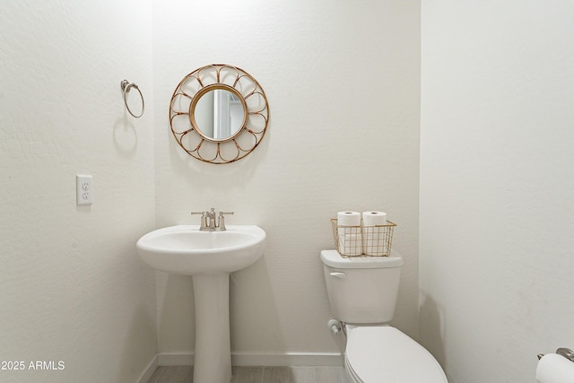 half bath featuring toilet, baseboards, and a sink