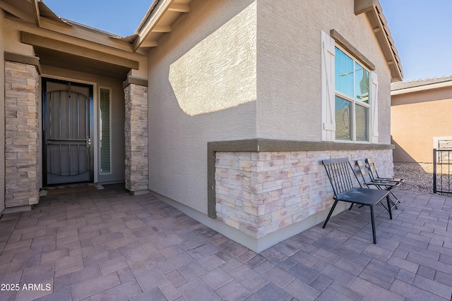 exterior space with a patio area, stone siding, and stucco siding