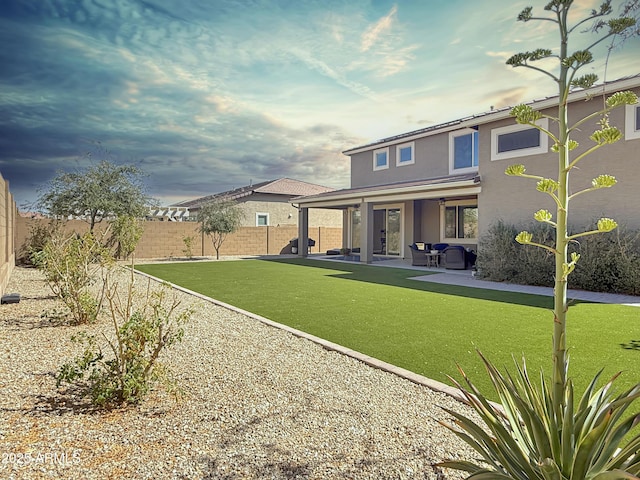 rear view of house with stucco siding, a yard, a fenced backyard, and a patio area