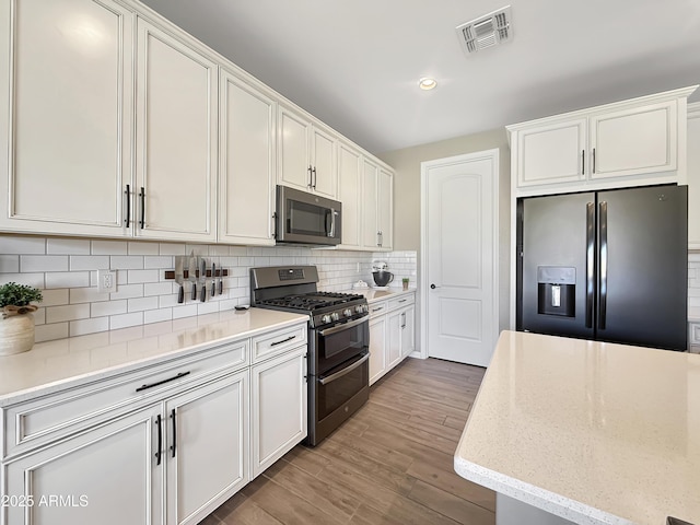 kitchen with white cabinets, tasteful backsplash, visible vents, and stainless steel appliances