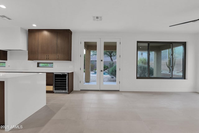 interior space with dark brown cabinetry, a wealth of natural light, beverage cooler, and french doors