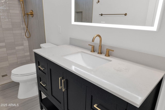 bathroom with vanity, toilet, hardwood / wood-style floors, and a tile shower