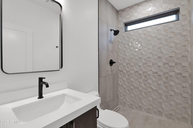 bathroom with vanity, tiled shower, and toilet