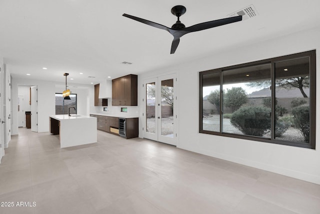 unfurnished living room featuring sink, wine cooler, ceiling fan, and french doors