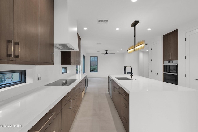 kitchen with wall chimney range hood, sink, hanging light fixtures, black electric cooktop, and stainless steel double oven