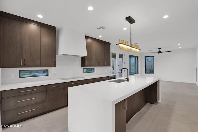 kitchen with premium range hood, sink, decorative light fixtures, an island with sink, and black electric stovetop