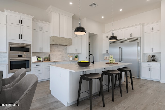 kitchen featuring white cabinets, appliances with stainless steel finishes, a center island with sink, and hanging light fixtures