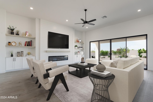 living room featuring built in features, a large fireplace, light hardwood / wood-style flooring, and ceiling fan